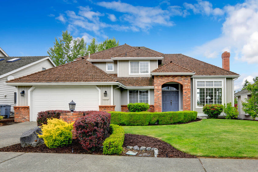 Classic house exterior with brick trimmed entrance porch, green lawn and trimmed hedges